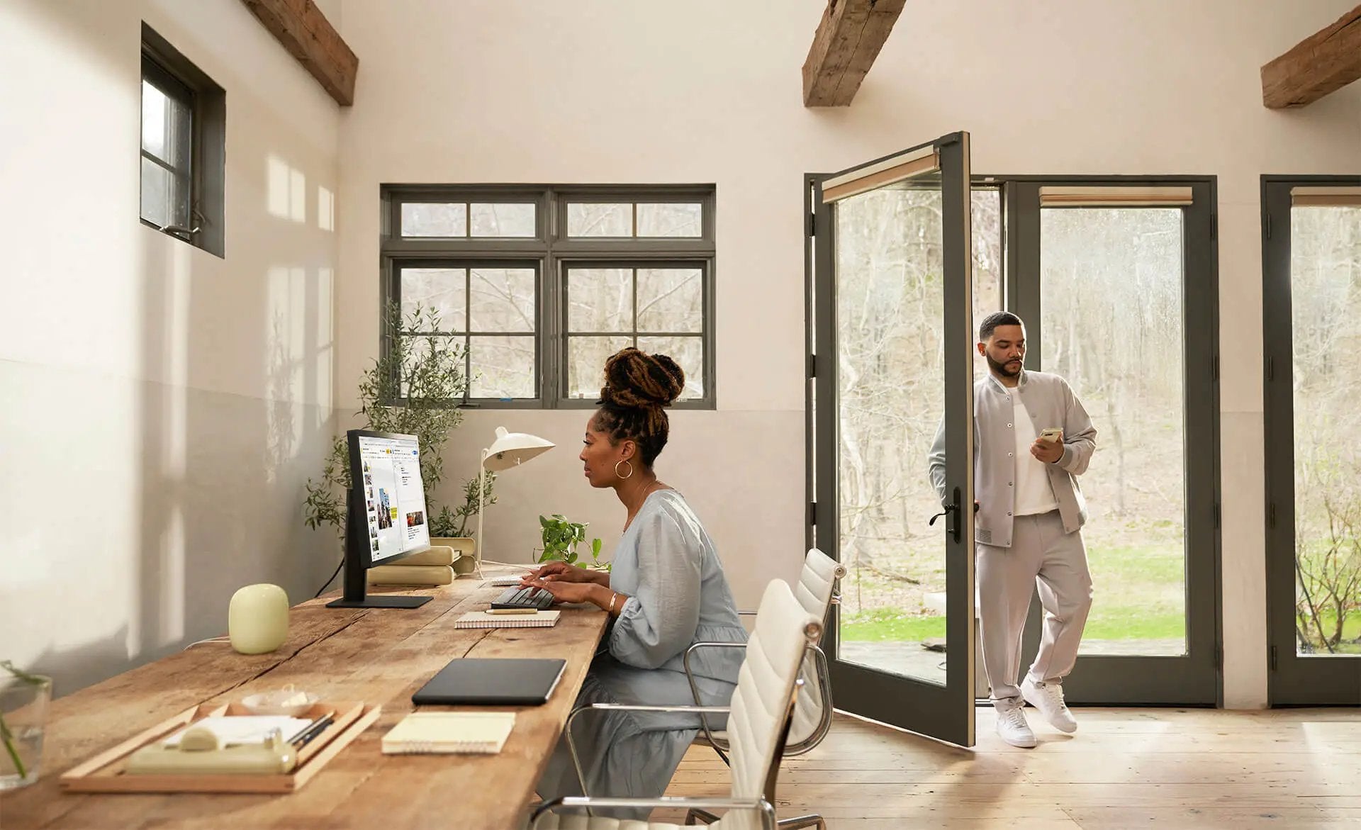 A man entering a home office while a woman works at her desk.